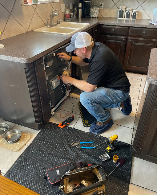 Appliance repair professional testing components behind a kitchen appliance